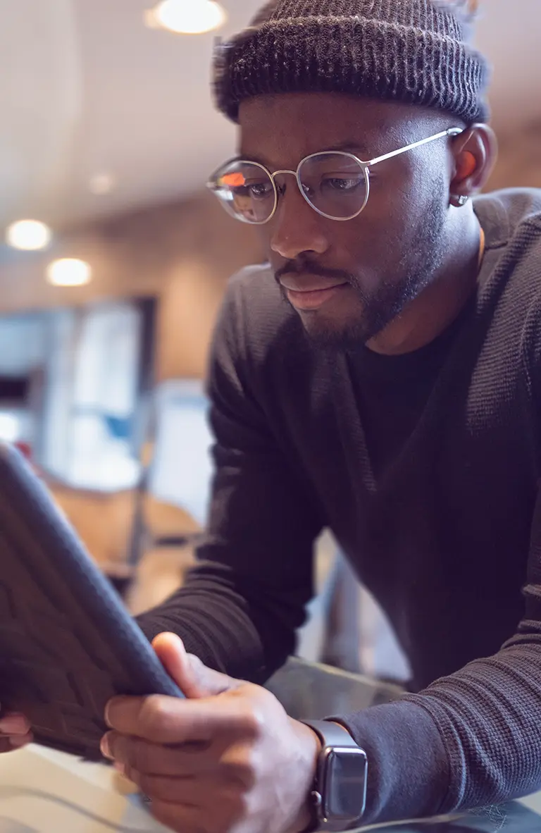 A young man in a knit cap and sweater works on a project on his tablet